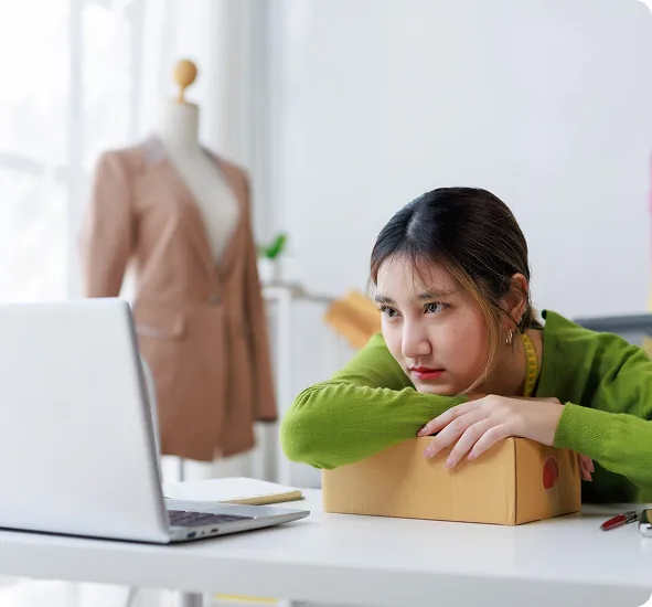 Online shop owner sat with a packed order, waiting on a Shopify store that has stopped keeping up